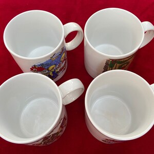 May include: Four white ceramic mugs with colorful holiday-themed illustrations. The mugs have a rounded shape and a handle on the right side.