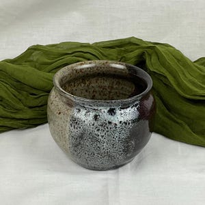 May include: A ceramic pot with a speckled brown glaze on the inside and a white and black speckled glaze on the outside.