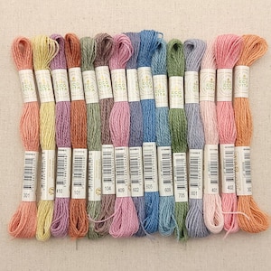 May include: A collection of 14 skeins of DMC Eco-Vita embroidery floss in various pastel colors, including peach, pink, lavender, blue, green, and yellow. Each skein is labeled with the DMC Eco-Vita logo and a number.