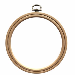 May include: A circular embroidery hoop constructed from light-toned wood, featuring a smooth finish and a metallic adjustment mechanism at the top. The hardware includes a small, ornate bronze-colored hanging loop attached to the screw.