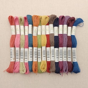 May include: A collection of 16 DMC Eco-Vita embroidery floss spools in various colors, including coral, pink, green, blue, orange, yellow, brown, red, purple, and indigo. Each spool has a white label with the DMC Eco-Vita logo and a number.