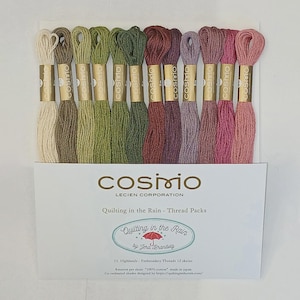 May include: A set of twelve Cosmo embroidery thread skeins in a gradient of green, brown, purple, and pink hues. Each skein features a gold label. The packaging displays the text Cosmo Lecien Corporation, Quilting in the Rain, and 8 meters per skein.
