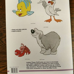 May include: A book cover featuring a colourful illustration of a seagull, a fish, a crab, and a dog. The book is titled "Golden Paper Doll" and includes the text "It's fun to dress the dolls in different clothes and dream up creative play situations."