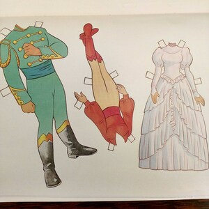May include: A paper doll set featuring three figures. The first figure is a man wearing a green uniform with gold trim. The second figure is a woman wearing a red and white dress. The third figure is a woman wearing a white dress with a ruffled skirt.