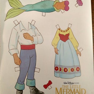 May include: Paper doll set featuring Ariel and Prince Eric from Disney's The Little Mermaid. The set includes a mermaid tail, a dress, a shirt, trousers, and a bow tie. The paper dolls are ready to be cut out and played with.
