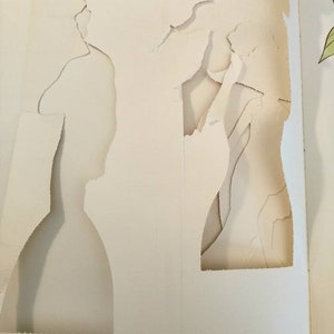 May include: A white book with two large holes cut out of the pages. The holes are shaped like people.