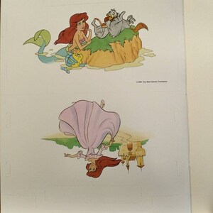 May include: A page from a children's book featuring a mermaid with red hair and a tail, a bird, and a fish. The bottom half of the page shows a woman with red hair wearing a pink dress, upside down, with a castle in the background. The text "&copy;1989 The Walt Disney Company" is at the bottom of the page.