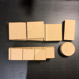 May include: A collection of light brown cardboard shapes including several square pieces, one rectangular piece, and one circular piece. The items are arranged in two rows, with the square and rectangular pieces stacked in groups and the circular piece placed separately.