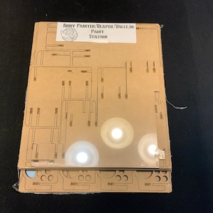 May include: A new paint station kit for miniature painting. The kit includes several laser-cut acrylic pieces with slots and cutouts for organizing paints and tools. The label reads "Army Painter/Reaper/Vallejo Paint Station."
