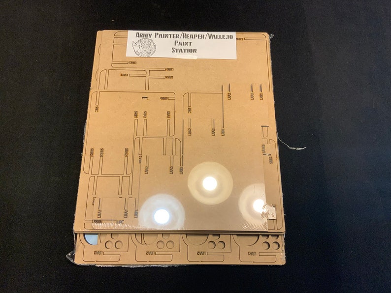 May include: A new paint station kit for miniature painting. The kit includes several laser-cut acrylic pieces with slots and cutouts for organizing paints and tools. The label reads "Army Painter/Reaper/Vallejo Paint Station."