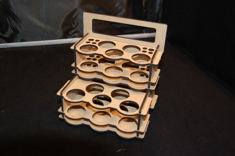 May include: A three-tiered wooden organizer with multiple circular and small rectangular openings. The top tier has a handle. The organizer is made of light-colored wood and appears to be designed for holding small items, such as paint bottles or art supplies.