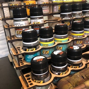 May include: A wooden paint bottle organizer with multiple shelves. The shelves are filled with small bottles of paint, some with labels that say "Worn", "Heavy", "Dust Effect", and "Fresh Mud".