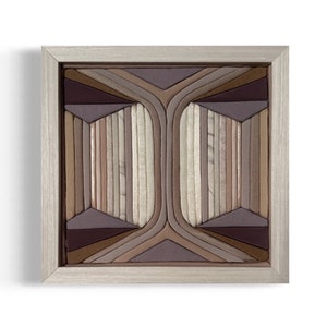 May include: A framed geometric wall art piece made of fabric strips in shades of brown, beige, and purple. The fabric is arranged in a symmetrical pattern, creating a modern and abstract design.