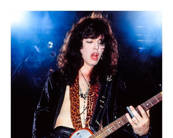 May include: A musician with long dark hair plays a silver and red electric guitar with a leopard print scarf around their neck.