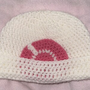 May include: White crocheted beanie with a pink crocheted circle design.