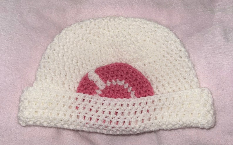 May include: White crocheted beanie with a pink crocheted circle design.