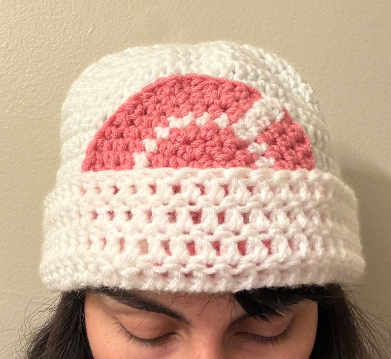 May include: White crocheted beanie with a pink and white crocheted design on the top.