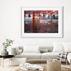 May include: A framed abstract painting with a white frame. The painting features a variety of colors, including red, orange, blue, and green. The painting is hung on a white wall above a white couch with pillows and a throw blanket.