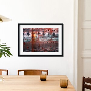 May include: Abstract painting in a black frame with red, orange, blue, and white colors. The painting is hanging on a white wall above a wooden table.
