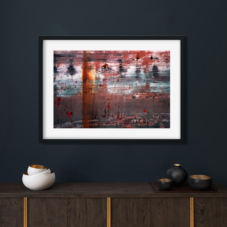 May include: Abstract art print in a black frame with a rusty, layered, and textured design in shades of red, orange, blue, and gray.