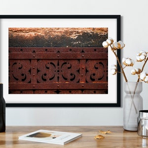 May include: A close-up of a rusty metal gate with a decorative pattern. The gate is made of metal bars with a decorative pattern cut out of them. The metal is rusty and has a brown color.