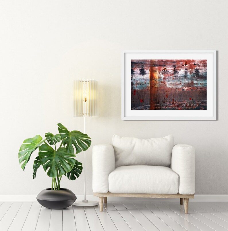 May include: A white armchair with a white lamp and a green plant in a black pot. A framed abstract painting with red, blue, and brown colors hangs on the wall behind the armchair.