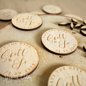 May include: Wooden save the date magnets with calligraphy script that reads "Save the Date Scott & Jo 22.09.2018".