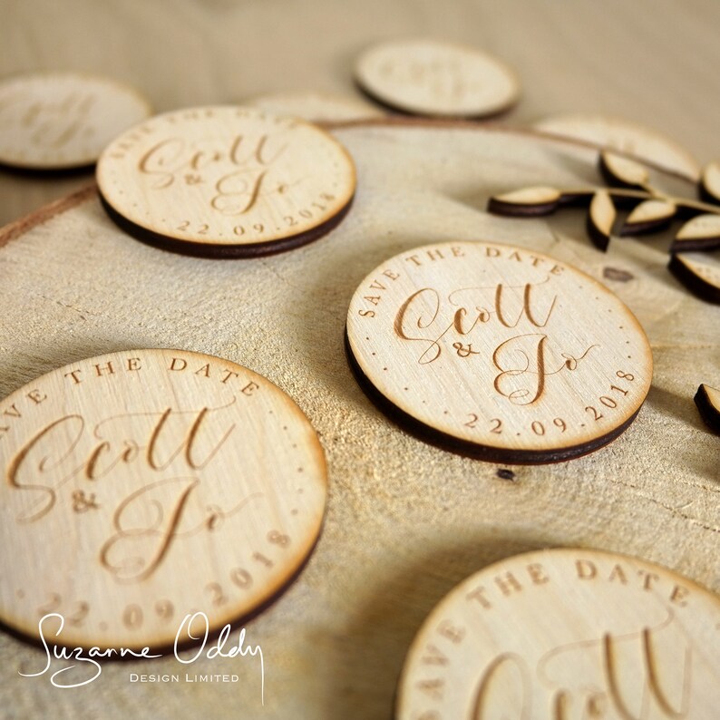 May include: Wooden save the date magnets with calligraphy script that reads "Save the Date Scott & Jo 22.09.2018".