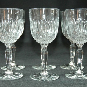 Puede incluir: Seis copas de vino de cristal transparente con un diseño de cristal tallado. Las copas tienen una copa redonda y un tallo largo y delgado.