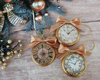 Peut inclure: Trois ornements de Noël dorés en forme d'horloges avec des cadrans en chiffres romains et des finitions dorées ornées. Les horloges ont des designs différents et sont décorées dans un style vintage.