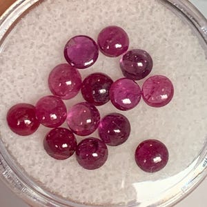 May include: A collection of round, pink gemstones in a clear plastic container. The gemstones are various shades of pink, from light to dark.