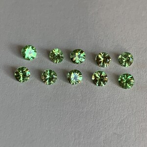 May include: Ten round, faceted green gemstones arranged in two horizontal rows. Each stone features a brilliant cut with light-reflecting surfaces, displaying various shades of lime and forest green with subtle yellow and gold highlights.