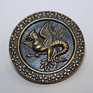 Puede incluir: Una taza de cerámica blanca con asa negra y el texto "But First, Coffee" en negrita negra. La taza se encuentra sobre un fondo borroso, resaltando su diseño limpio.