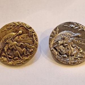 May include: Two antique brass buttons with detailed relief designs. One button is gold-toned, the other silver-toned. Each features a bird, a figure, and landscape elements, likely from a historical era.