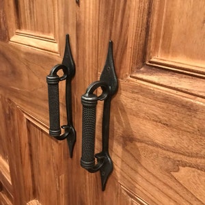 Könnte beinhalten: Zwei schwarze Metall-Türgriffe mit einem dekorativen Design. Die Griffe sind an einer Holztür befestigt.