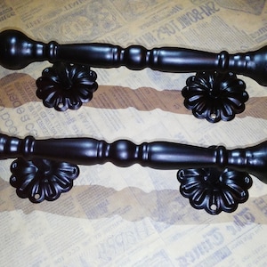 以下が含まれることがあります： 装飾的な花柄のついた黒い金属製のドアノブが2つ。ノブは丸みを帯びた端と長く円筒形の本体を持っています。