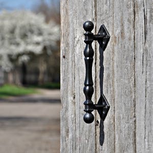Peut inclure: Poignée de porte en métal noir avec un design arrondi, montée sur une porte en bois vieilli.