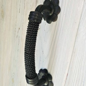 Könnte beinhalten: Schwarzer Türknauf aus Metall mit einem seilartigen Design und dekorativen, blumenförmigen Enden.