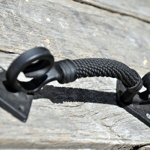 May include: Black metal door handle with a rope design. The handle is attached to a square metal plate.
