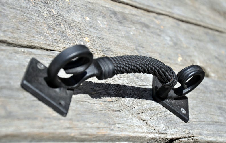 May include: Black metal door handle with a rope design. The handle is attached to a square metal plate.