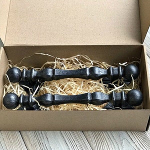 May include: Two black metal drawer pulls with rounded ends, packaged in a brown cardboard box with shredded paper packing material.
