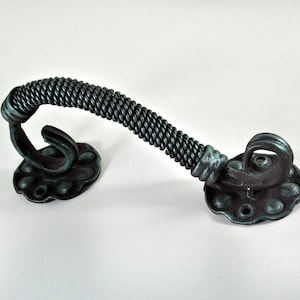 以下が含まれることがあります： 濃い緑色の仕上げが施された装飾的なドアハンドル。ハンドルはねじれたロープのデザインで、2つの装飾的な花型のベースプレートに取り付けられています。金属製の金具は、使い古されたアンティークな外観をしています。