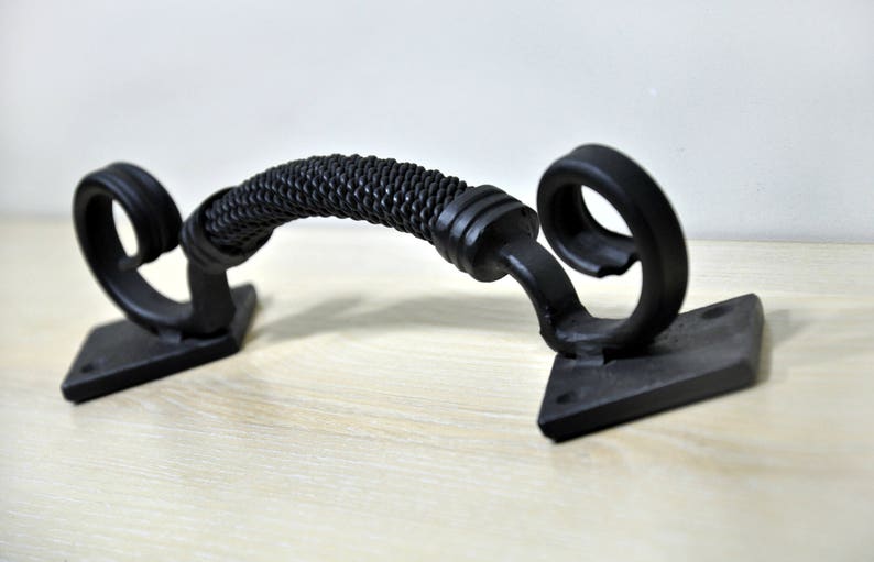 May include: Black metal door handle with a braided design on the handle and a scroll design on the ends. The handle is mounted on two square plates.