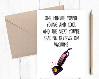 以下が含まれることがあります： 「One minute you're young and cool and the next you're reading reviews on vacuums」と黒文字で書かれた白いカード。カードの下部には、ピンクの掃除機の漫画イラストが描かれている。