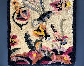 May include: A hand-hooked rug with a floral design. The rug features a variety of flowers in shades of pink, red, yellow, and blue, set against a cream background. The rug is bordered with a black fringe.
