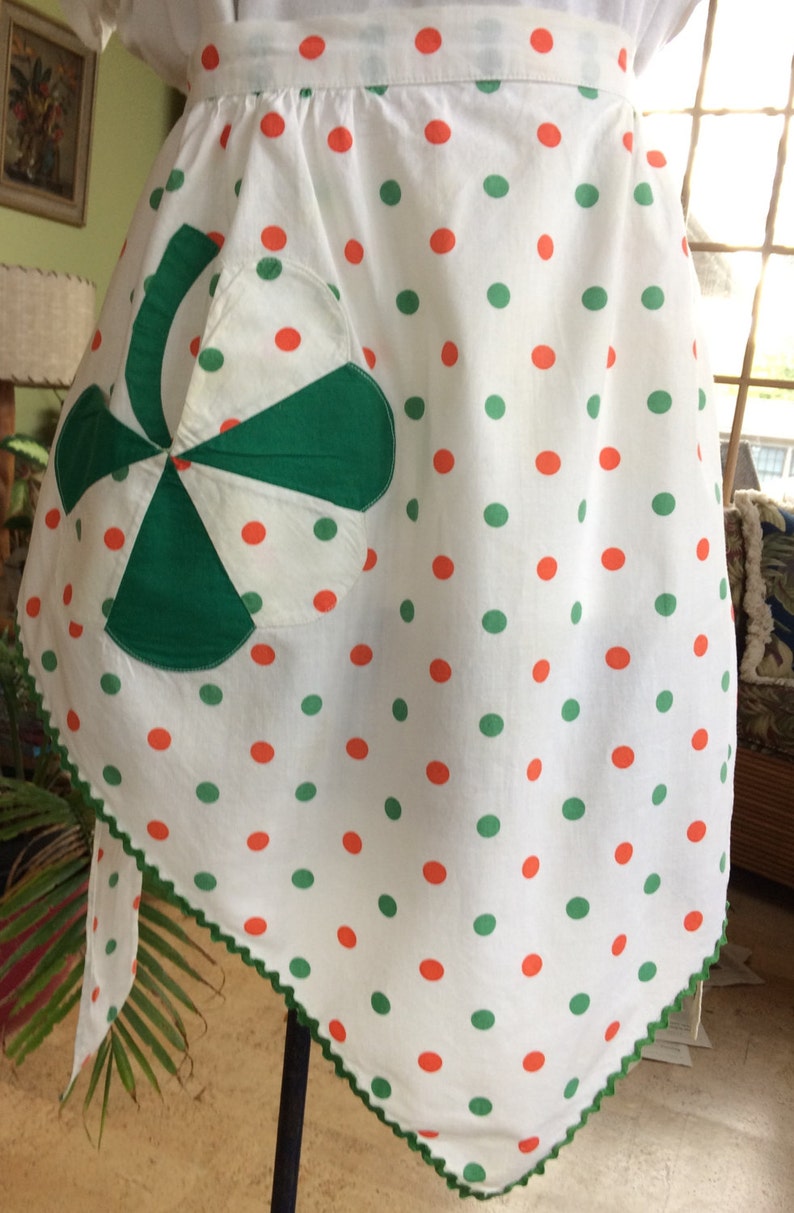 May include: A white apron with green and orange polka dots. The apron has a green and white patchwork pocket in the shape of a pinwheel.