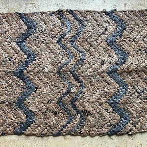 May include: A brown and blue woven rug with a zig-zag pattern. The rug has a scalloped edge.