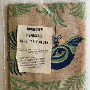 May include: A brown and green disposable card table cloth with a blue and green Christmas ornament design. The package includes instructions that say "Nonwoven Disposable Card Table Cloth" and "Do Not Wash - This material will lose its fire resistance if washed or dry cleaned."