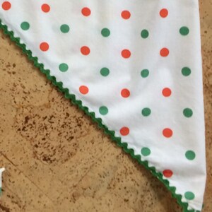 May include: A white fabric triangle with a green scalloped edge. The fabric has a repeating pattern of red and green polka dots.
