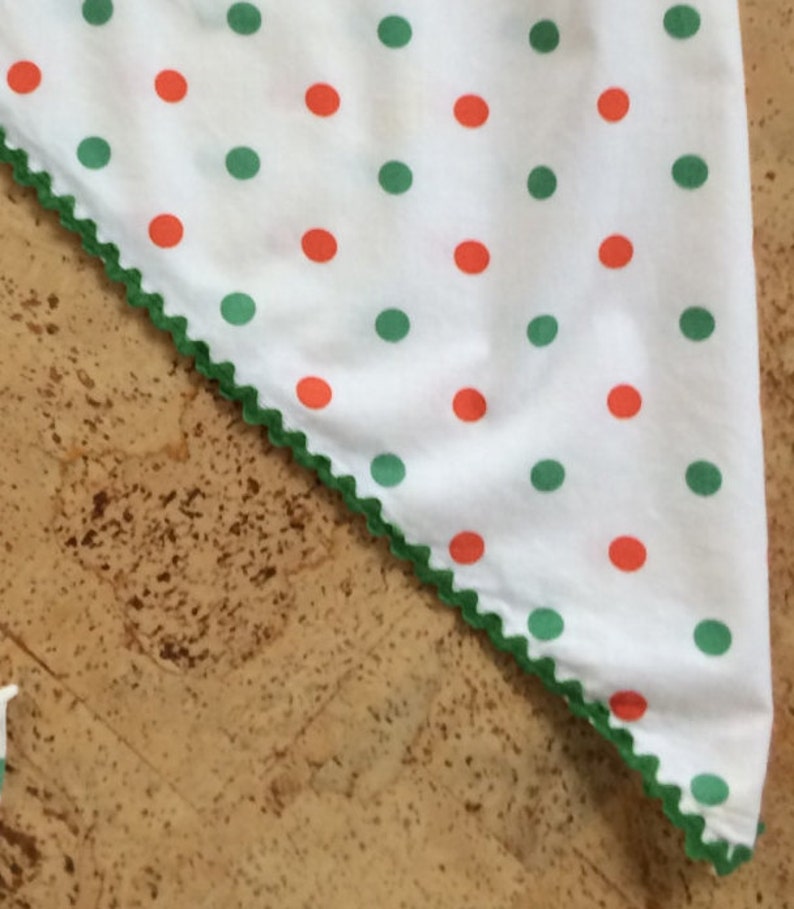 May include: A white fabric triangle with a green scalloped edge. The fabric has a repeating pattern of red and green polka dots.
